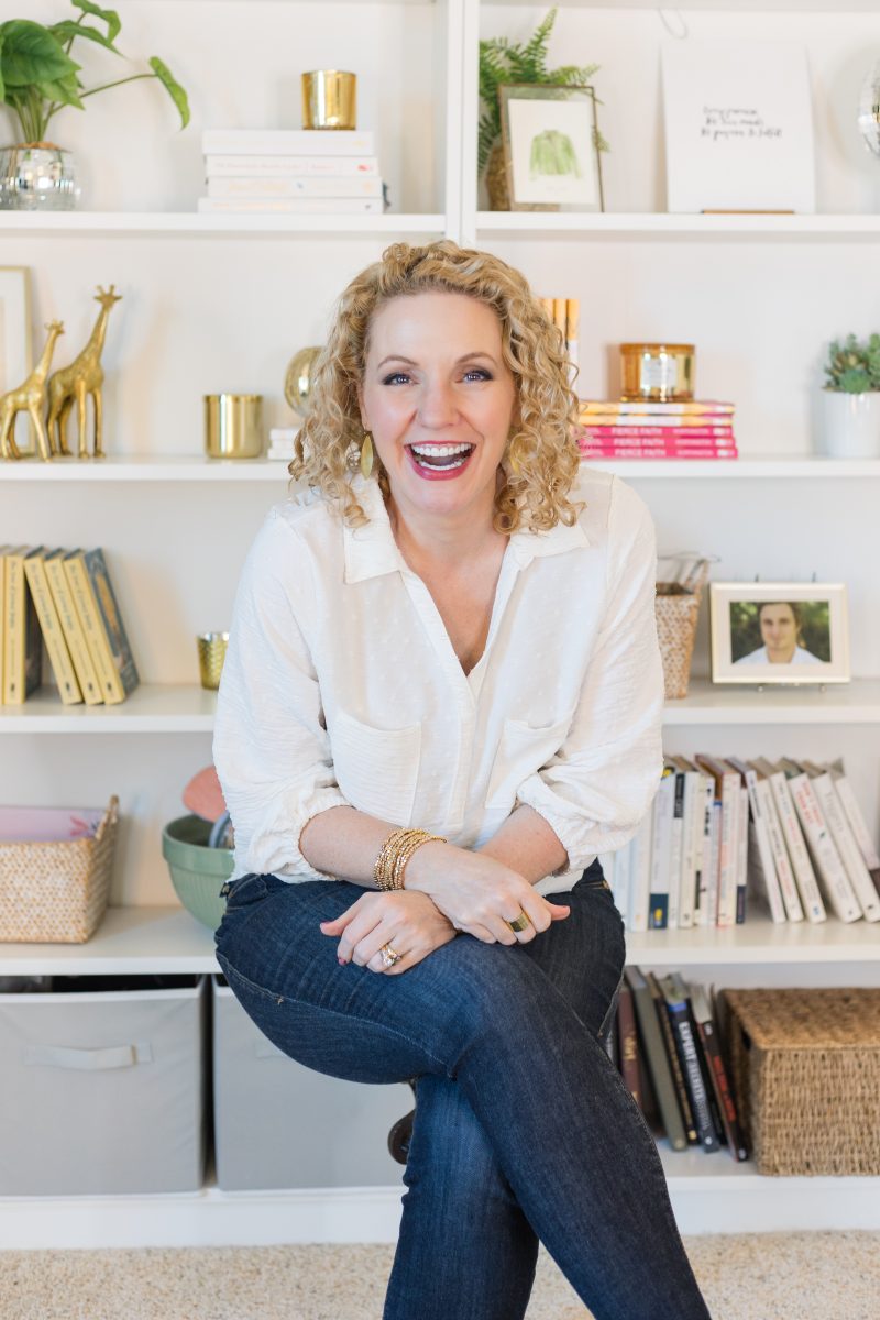 Alli Worthington sitting in front of white bookshelves